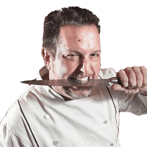 The Fiery Chef playfully holding a kitchen knife between his teeth in chef’s whites