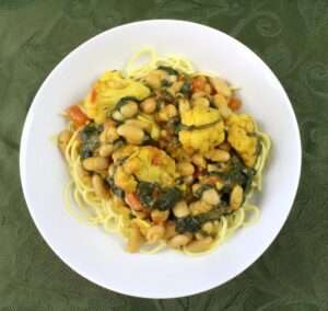 Curried roasted cauliflower, white beans, and spinach served over spaghetti noodles in a white bowl