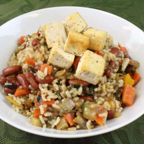 Dirty brown rice with vegetables and tofu cubes in a white bowl