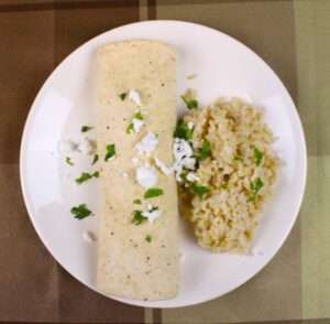 Cabbage burrito served with a side of rice on a white plate